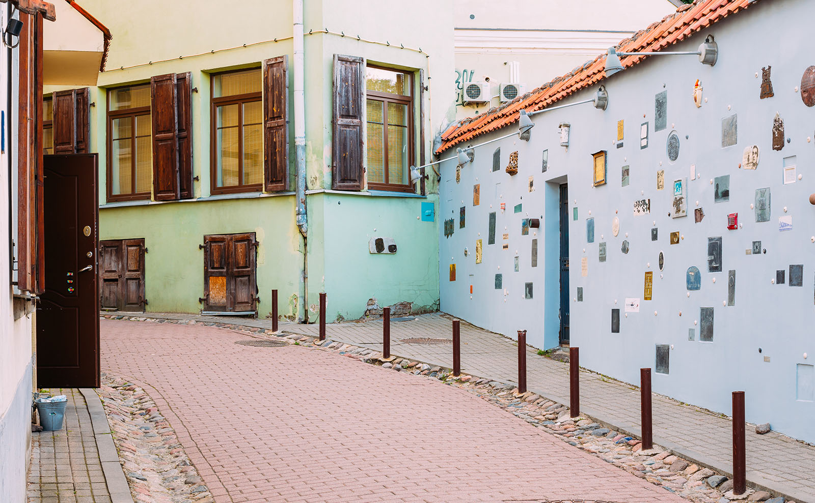 cobblestone alley on a cloudy day with a light blue wall decorated with small plaques