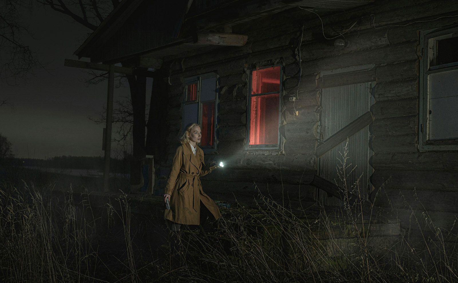 blonde woman outside a scary looking house at night with a flashlight
