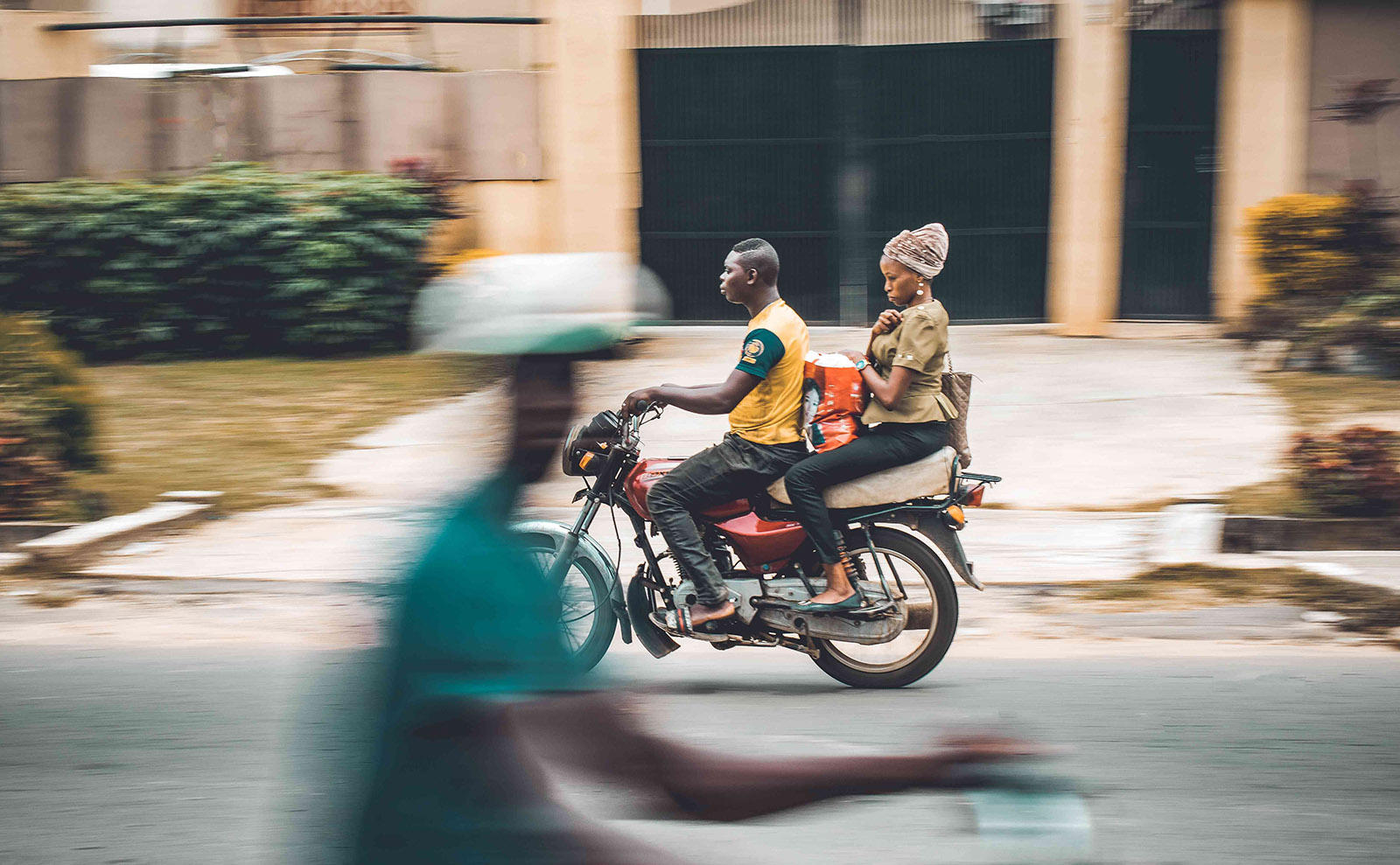 nigerian man and woman riding a scooter on a residential street