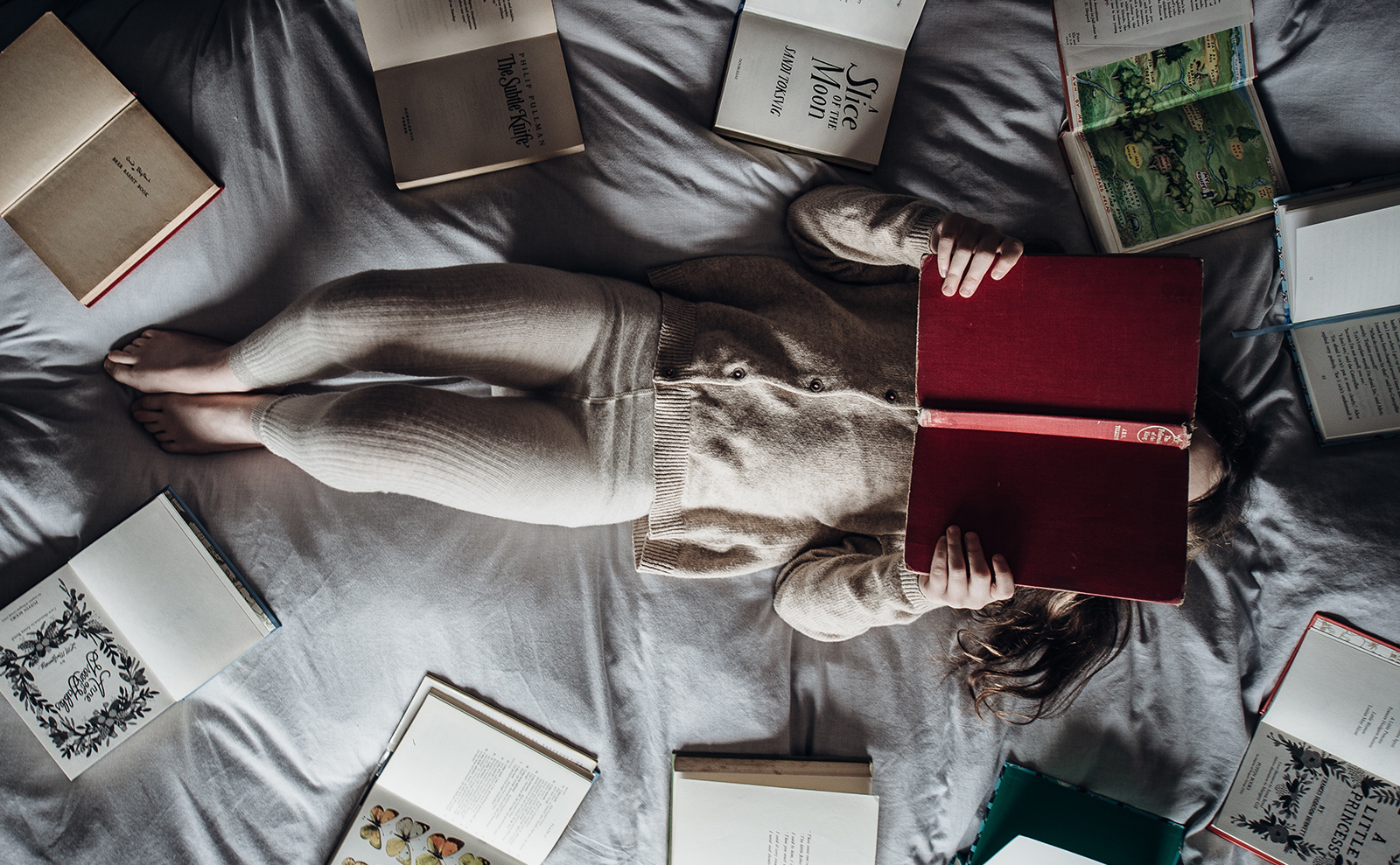a young girl lying on a bed surrounded by books