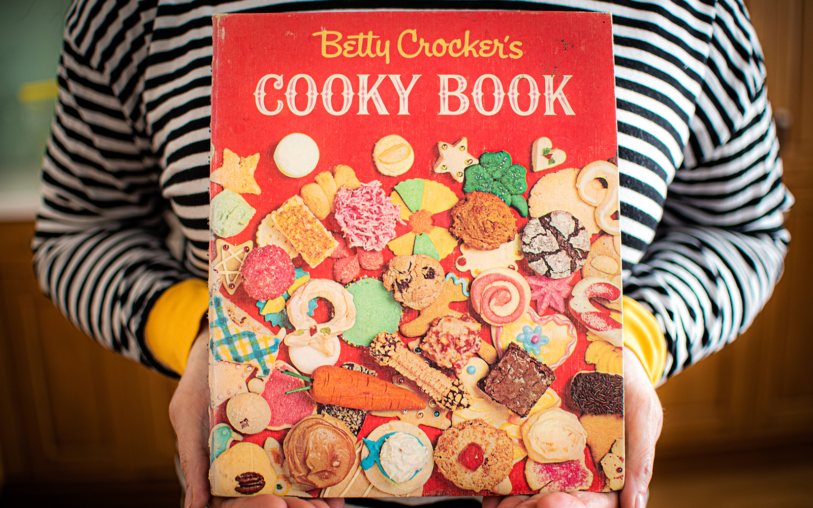  close-up of the cover of betty crocker's cooky book held by someone wearing a black and white striped shirt
