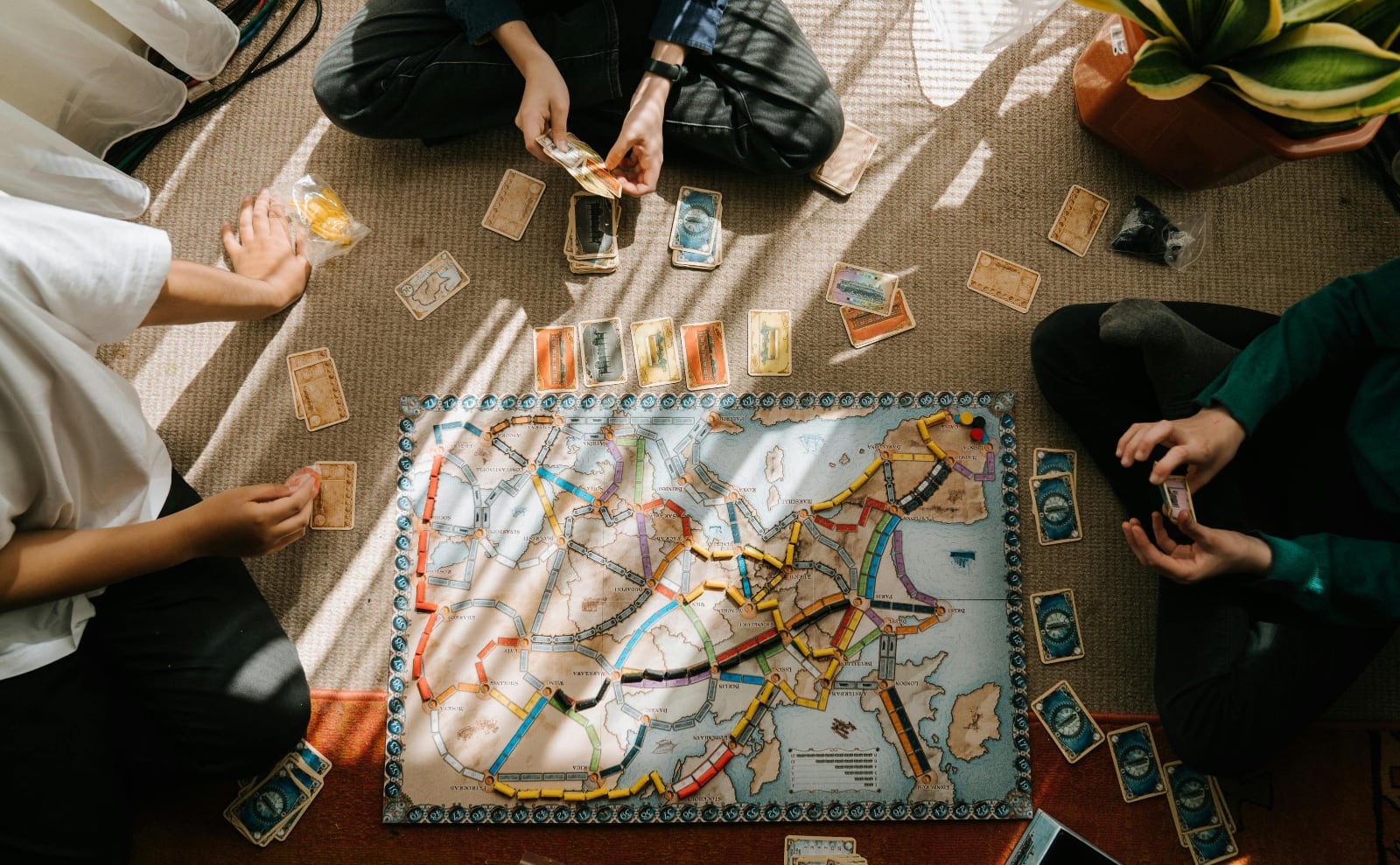 three people sit on the floor on a rug playing a board game with cards and dice