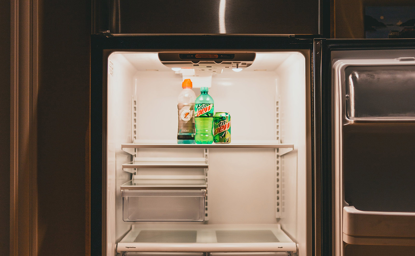 a fridge with the door standing open with nothing inside except three bottles of Mountain Dew