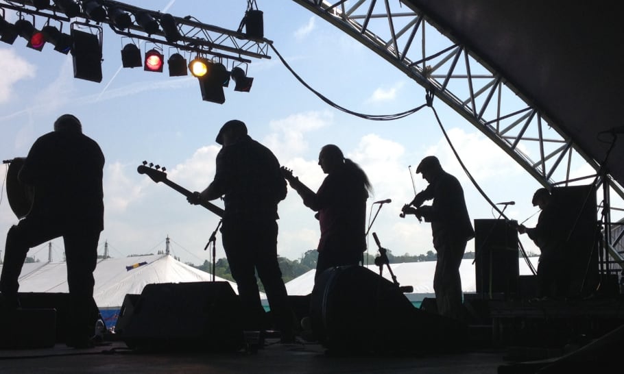 five musicians standing in a diagonal line on stage with instruments