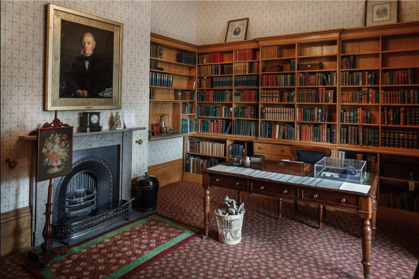 victorian library with desk and bookshelves filled with red and blue books