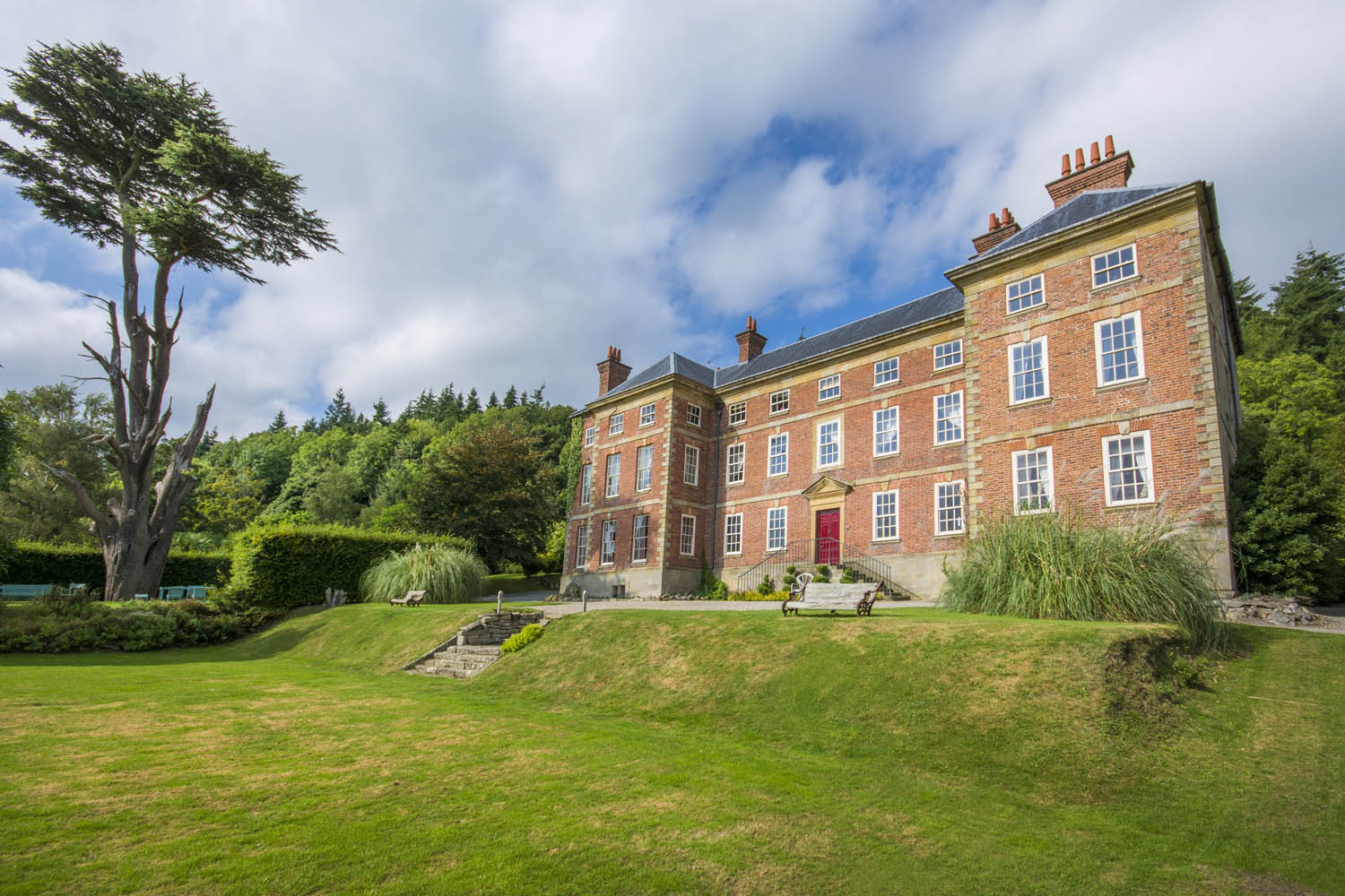 facade of a red brick georgian manor house surrounded by trees and green lawn