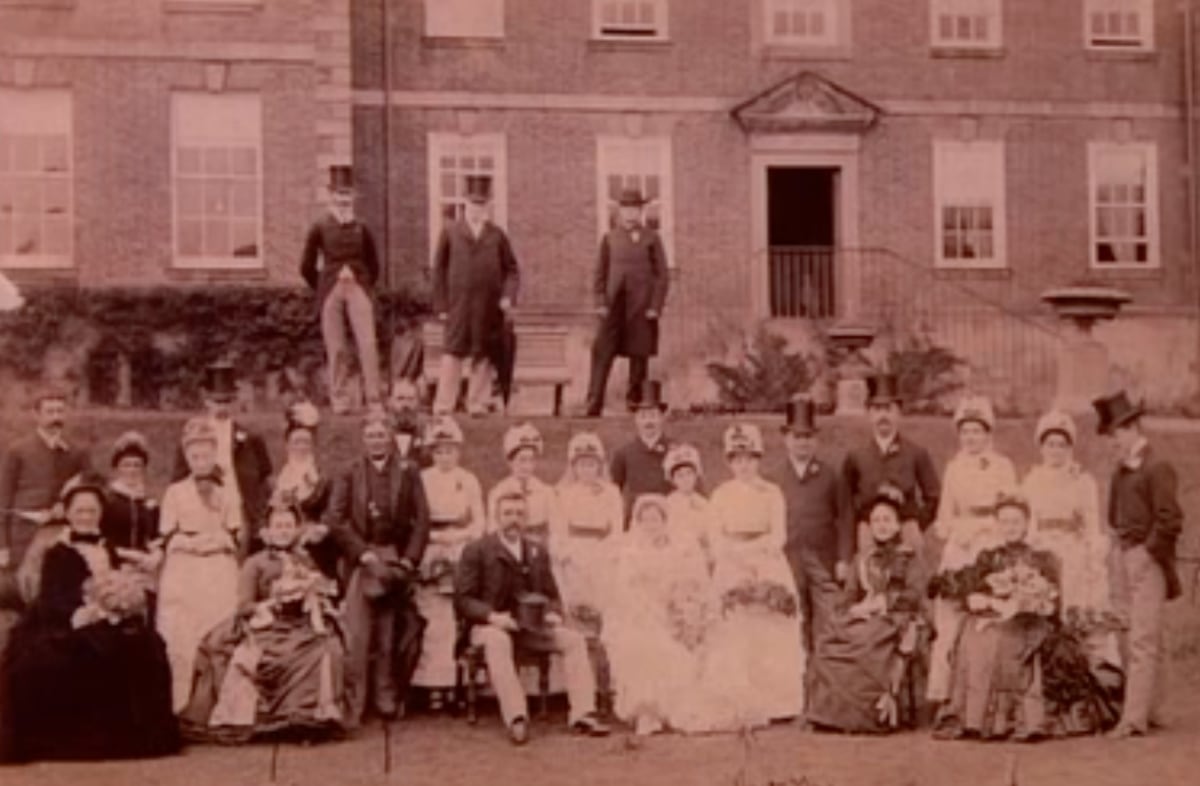 vintage photo of victorian family and staff posed for a photo on a grass lawn