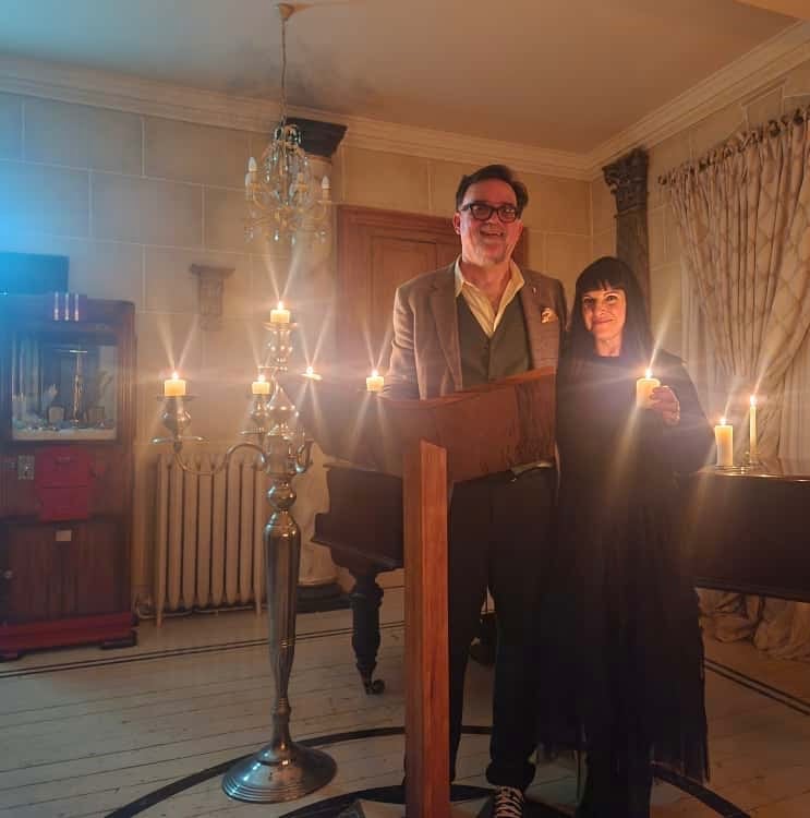 man and woman holding candles next to a grand piano