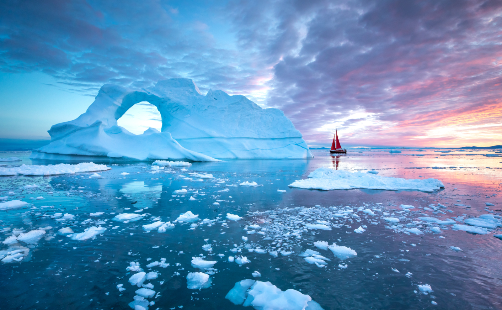 a red sailboat bloats next to an iceberg in the arctic