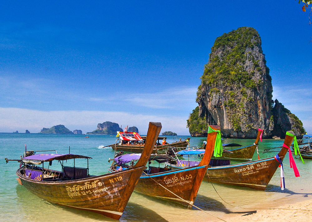 wooden boats with colorful flags sitting on the sand at phra nang beach