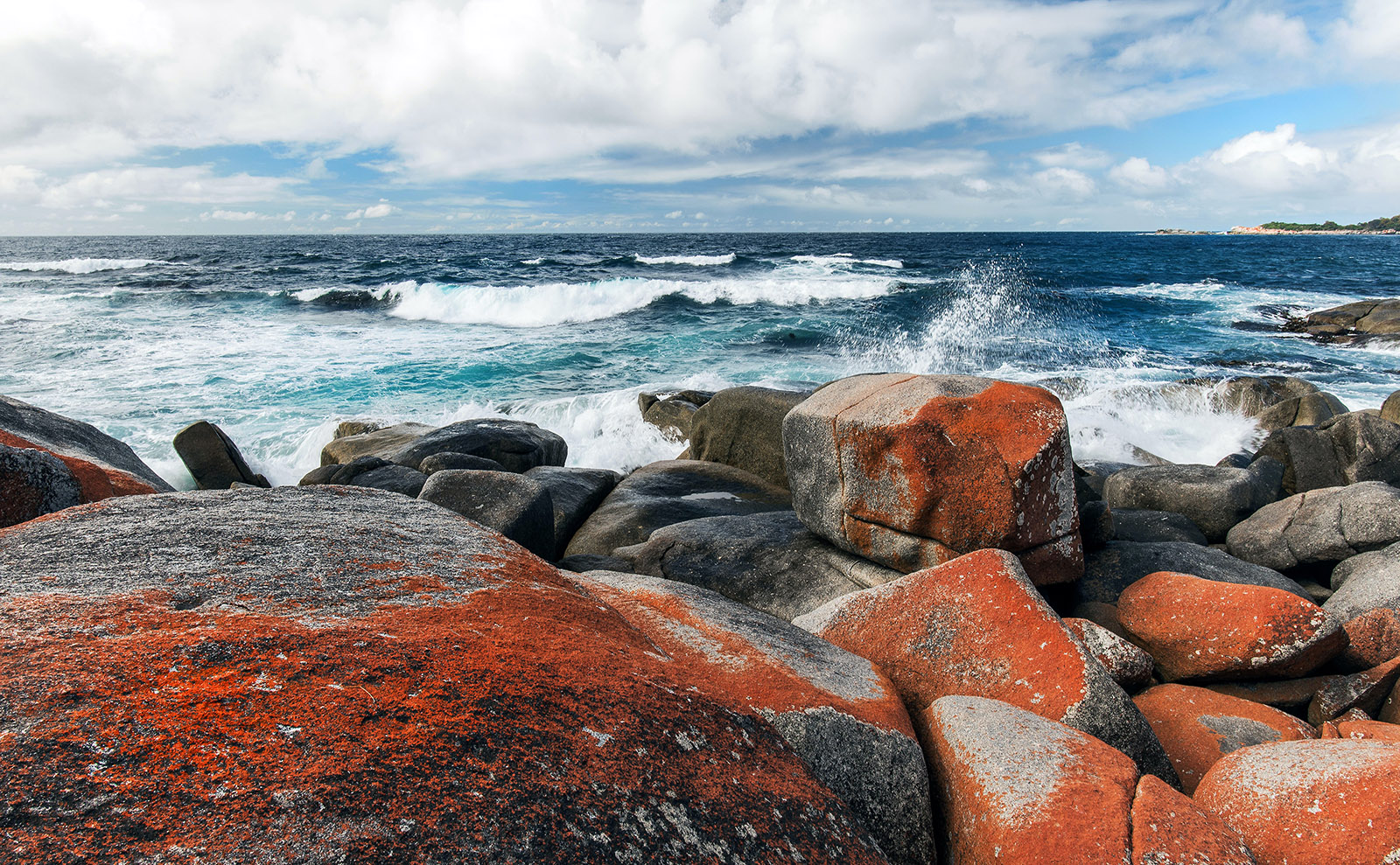  gray rocks with orange lichen and dark blue waves of water