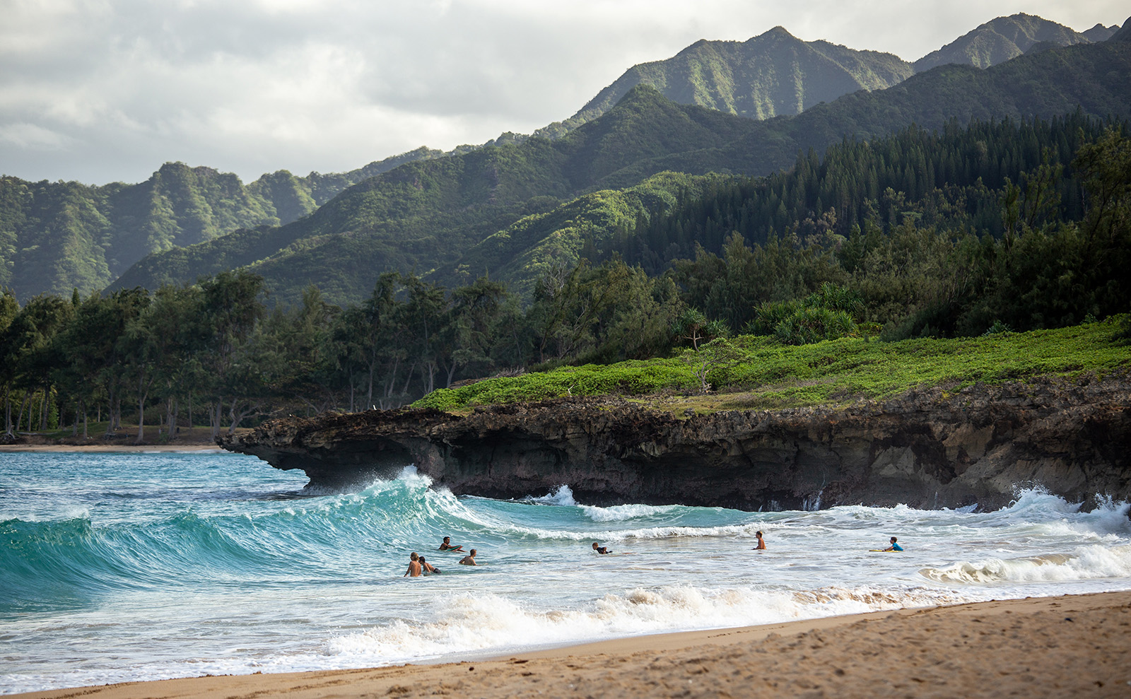 people swimming in the blue water on a hawaiian beach with green mountains in the background