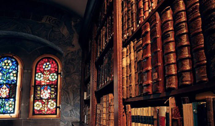 close up of leather bound books on wooden bookshelves with stained glass windows in the background
