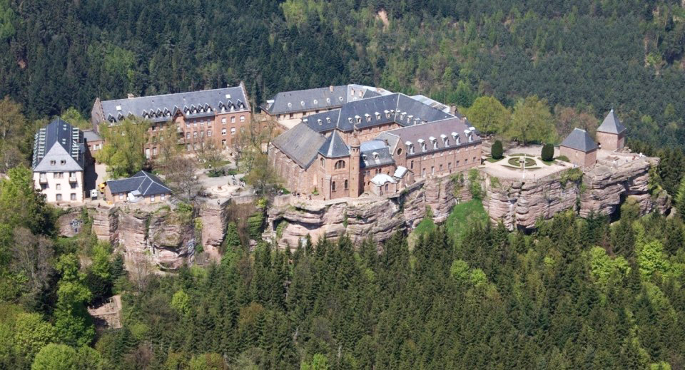 red stone buildings on a mountaintop surrounded by forest
