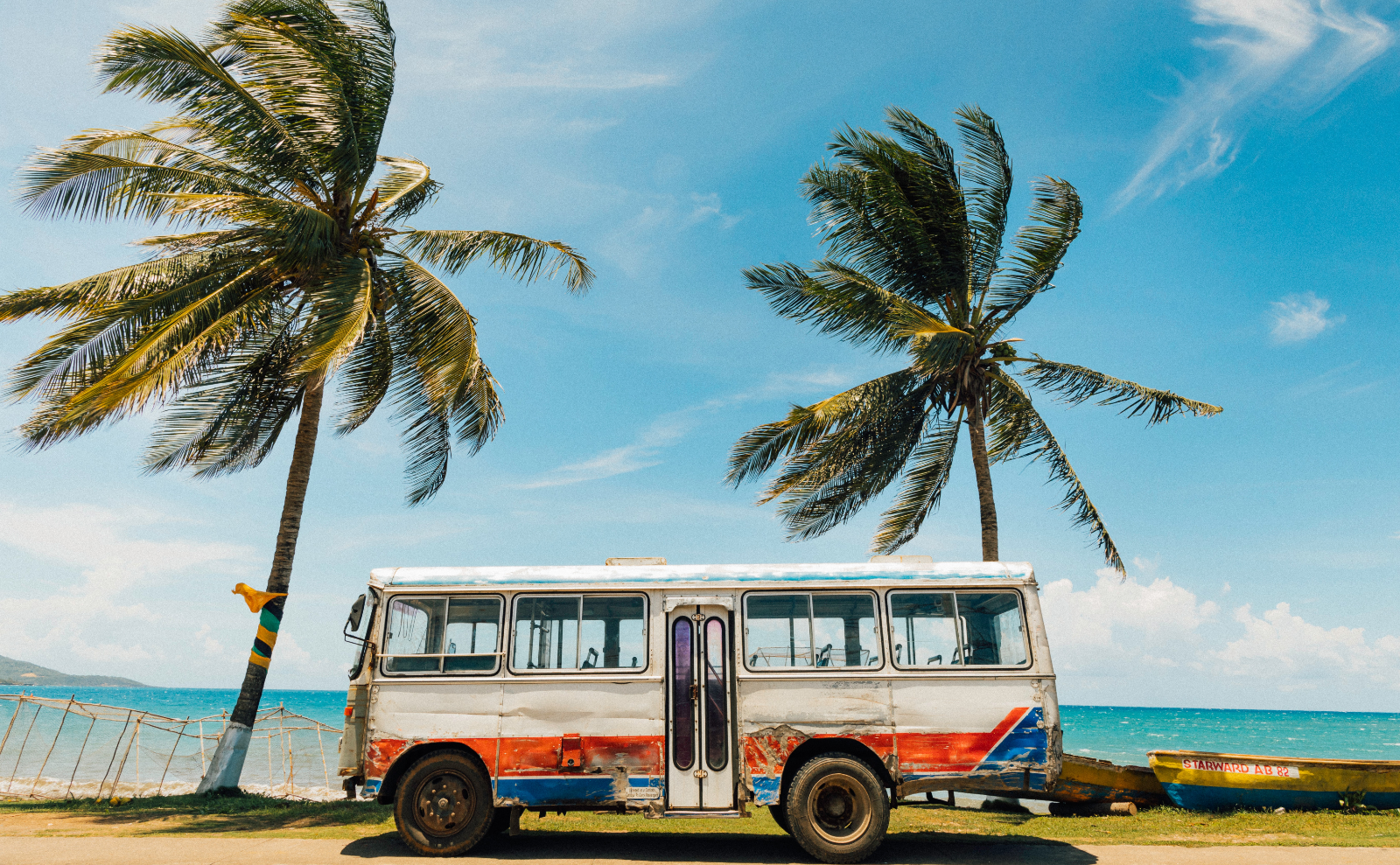 a vintage bus parked between two palm trees next to the beach on a sunny day
