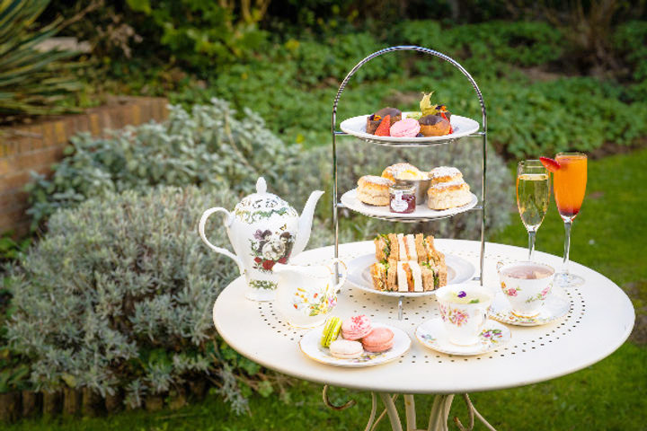 table set in a garden with an afternoon tea with a tiered serving dish and teacups