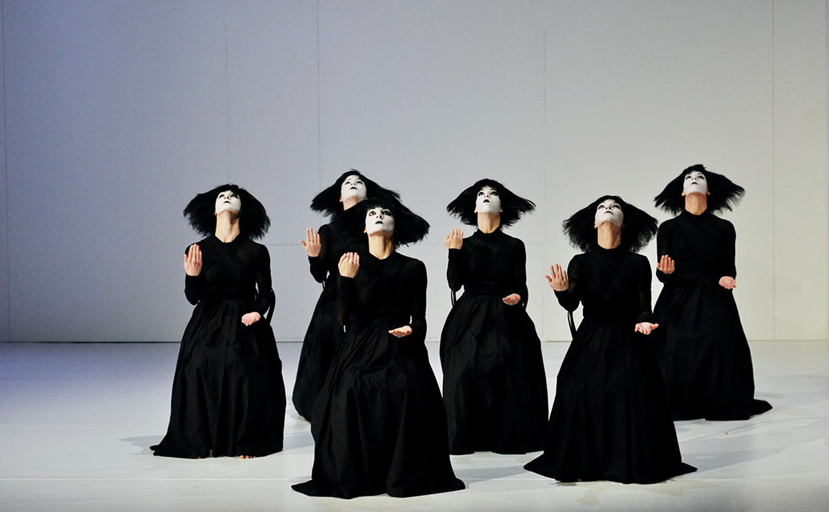 a group of women on a stage in black gowns and white face paint