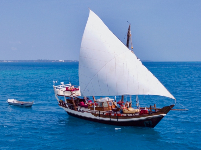wooden boat with a white sail on blue water