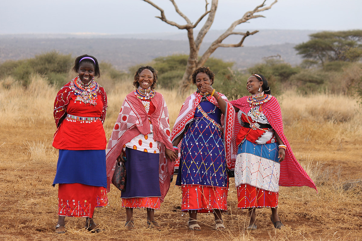 a group of maasai women smile and pose for a photo wearing traditional red and blue attire