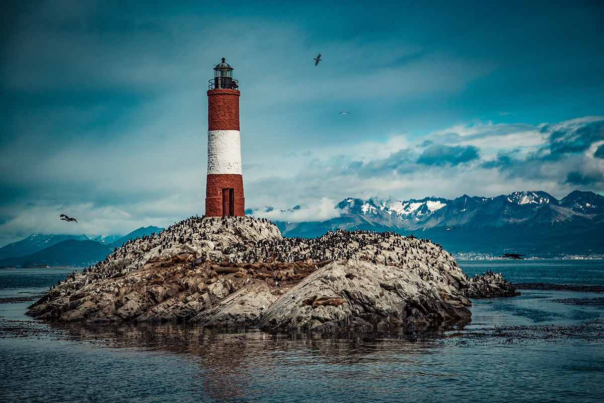 red and white lighthouse on a small island surrounded by water and mountains