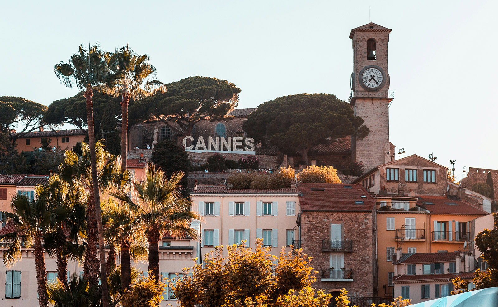 pastel colored houses on a hill with a sign that says cannes in big white letters