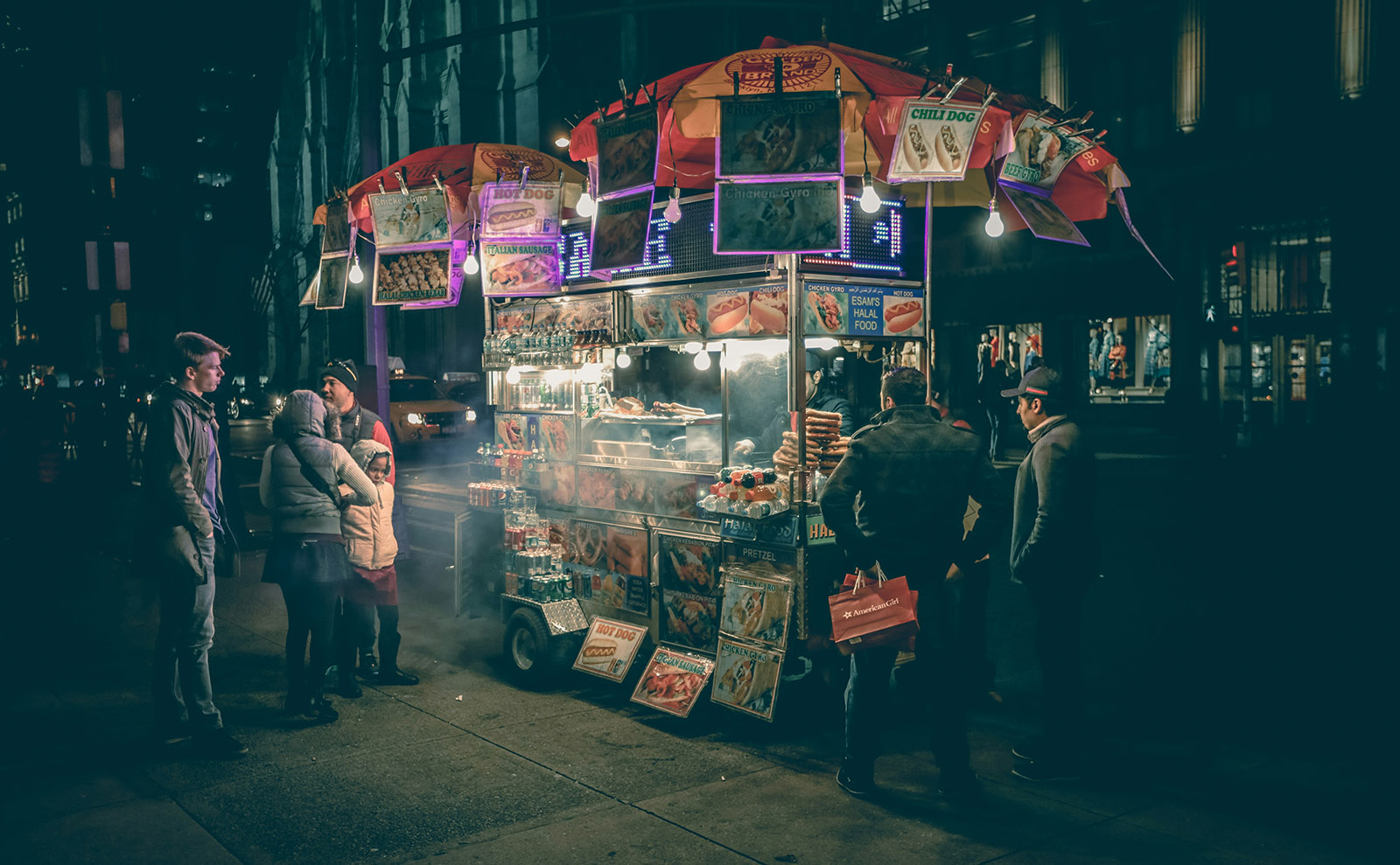 nighttime view of a hot dog cart in new york city covered with pictures of food and flags