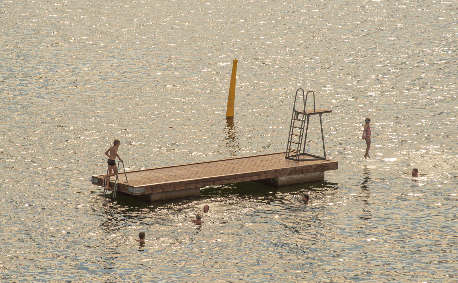 kids swimming around a wooden raft in the middle of blue water