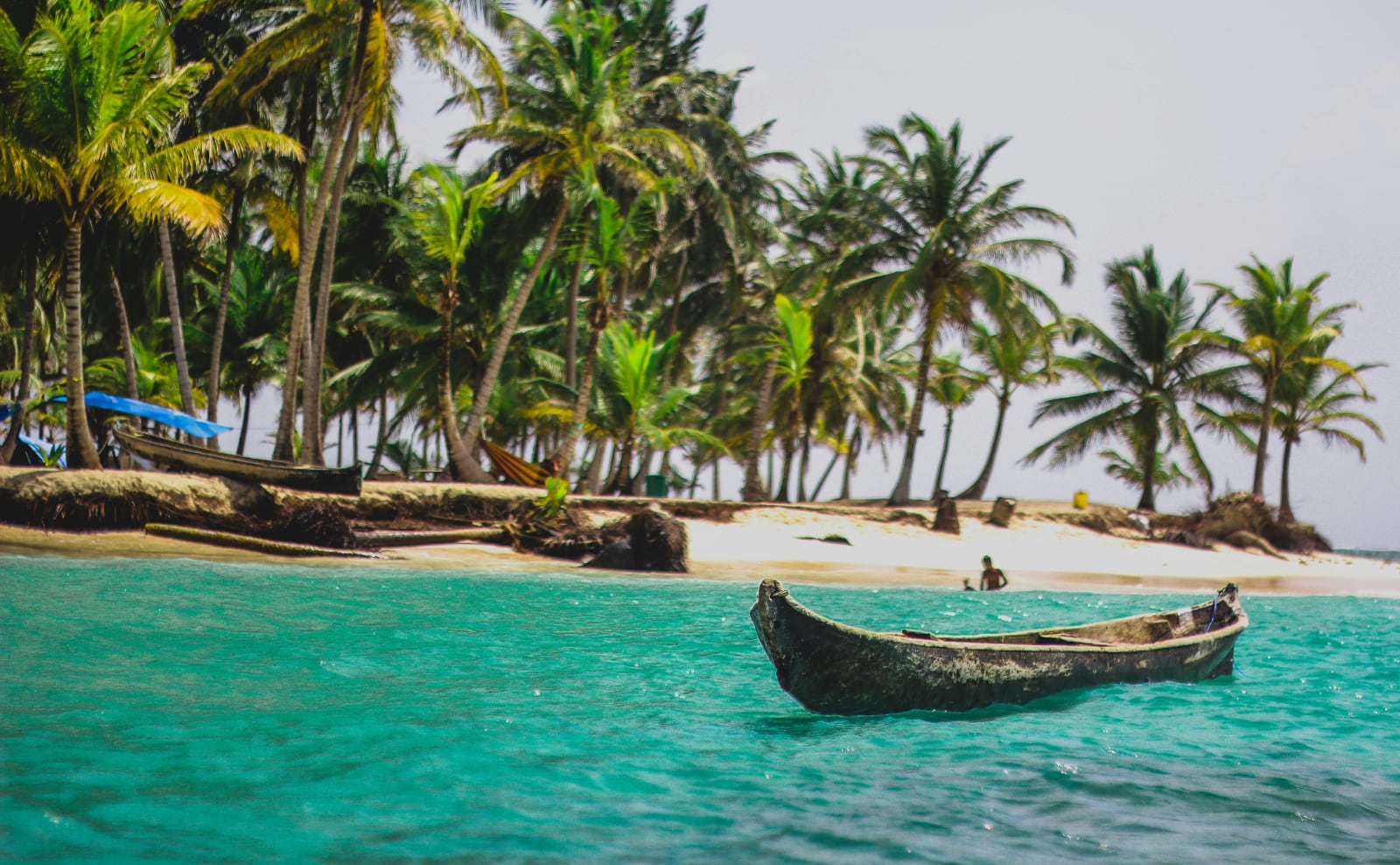 handmade canoe floating in turquoise blue water off the coast of an island with palm tree