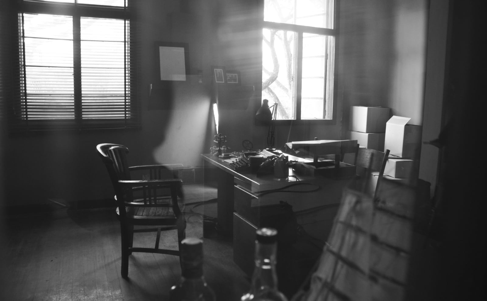 black and white photo of an office with a wooden desk and light coming in through thin window blinds