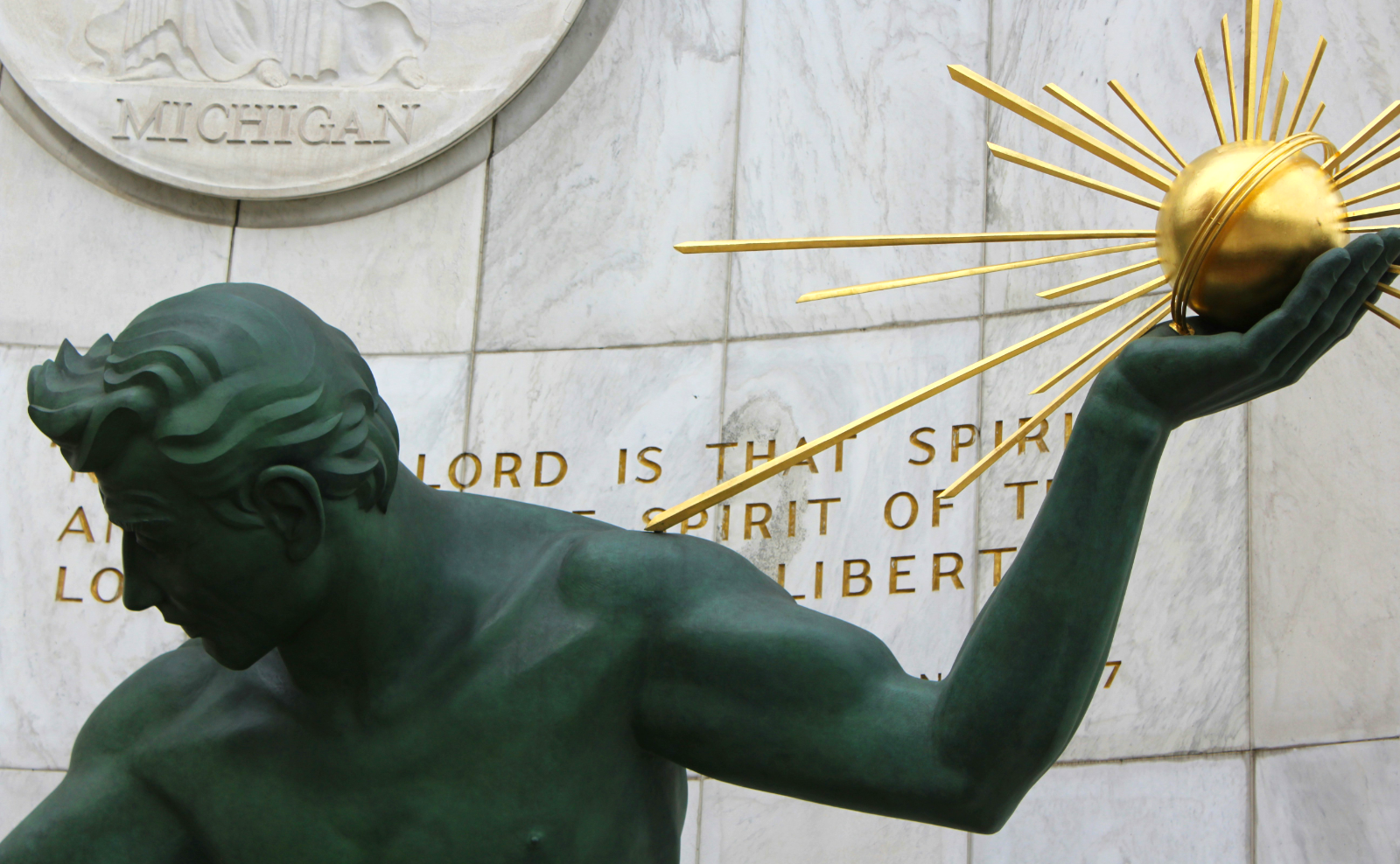 close up of the head and arm of bronze statue holding a shiny gold orb emitting rays