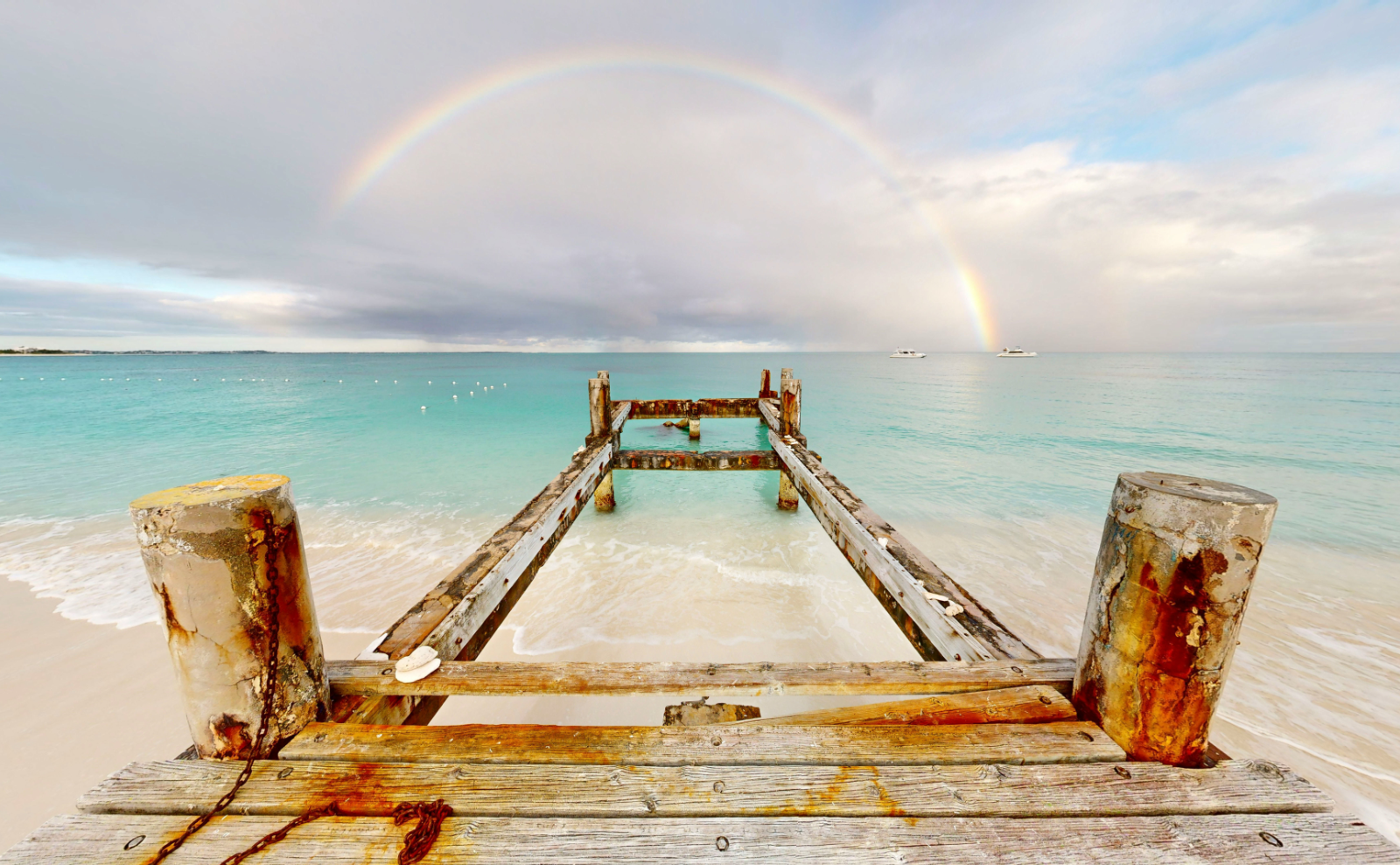a wooden dock stretching out into very clear turquoise blue water with a rainbow arching in the background