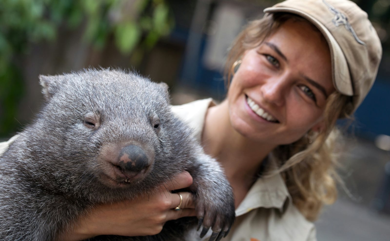 a young woman holding a wombat in a hug looking at the camera