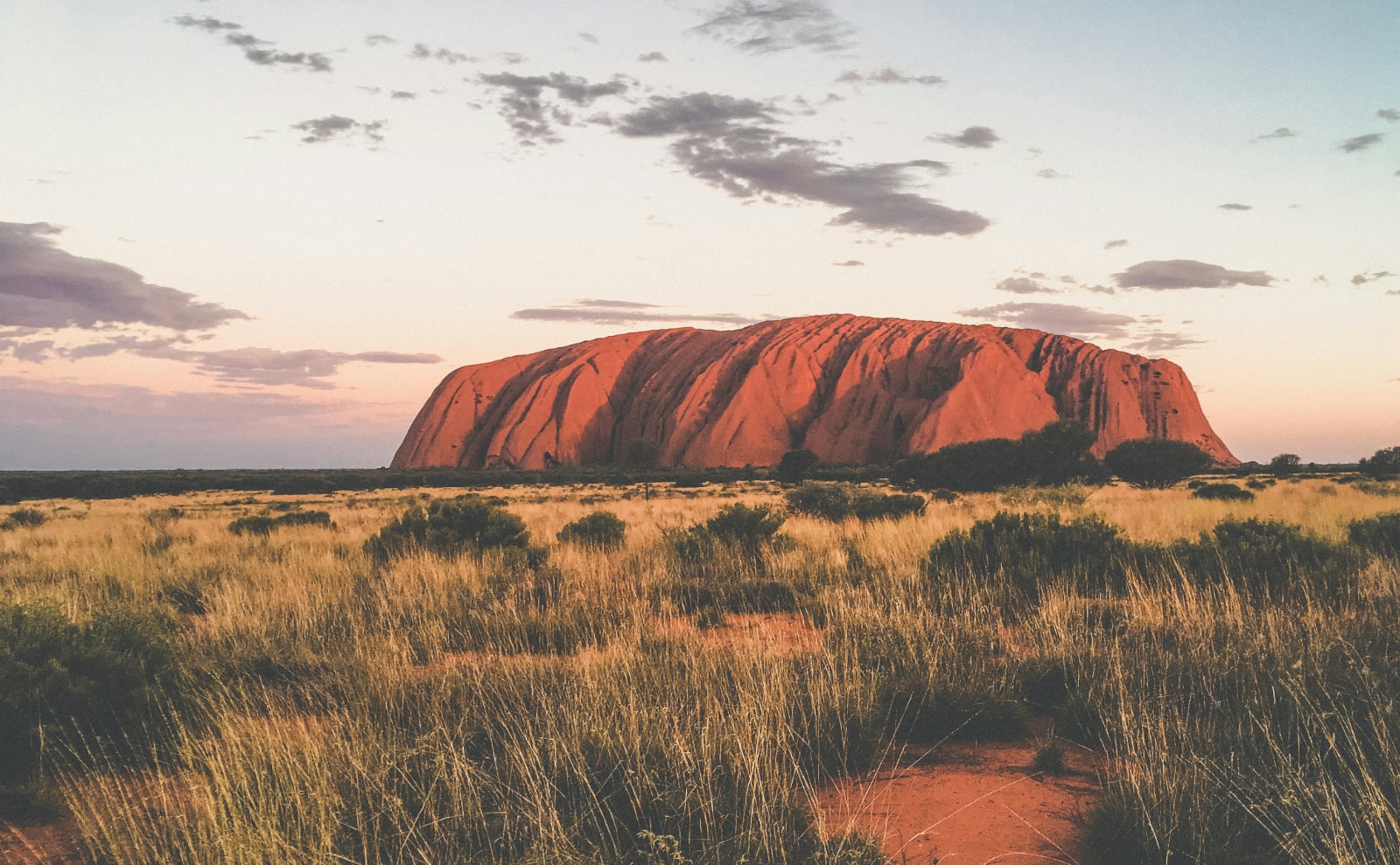 a large red rock in the middle of a flat desert