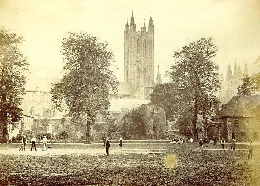 black and white photo of young men playing cricket on a grassy field in the 19th century