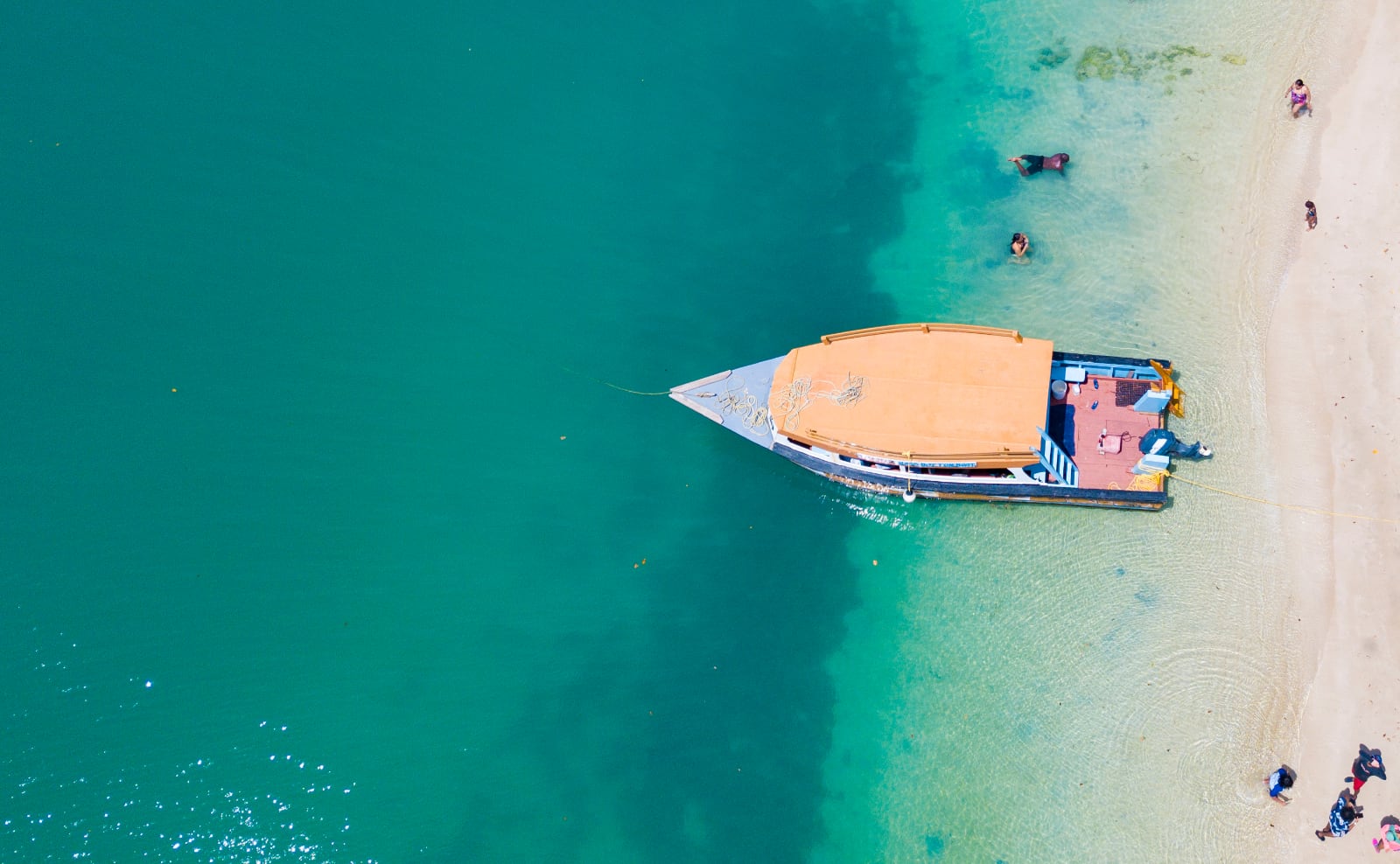 an overhead view of a wooden boat stretching out into very clear turquoise blue water