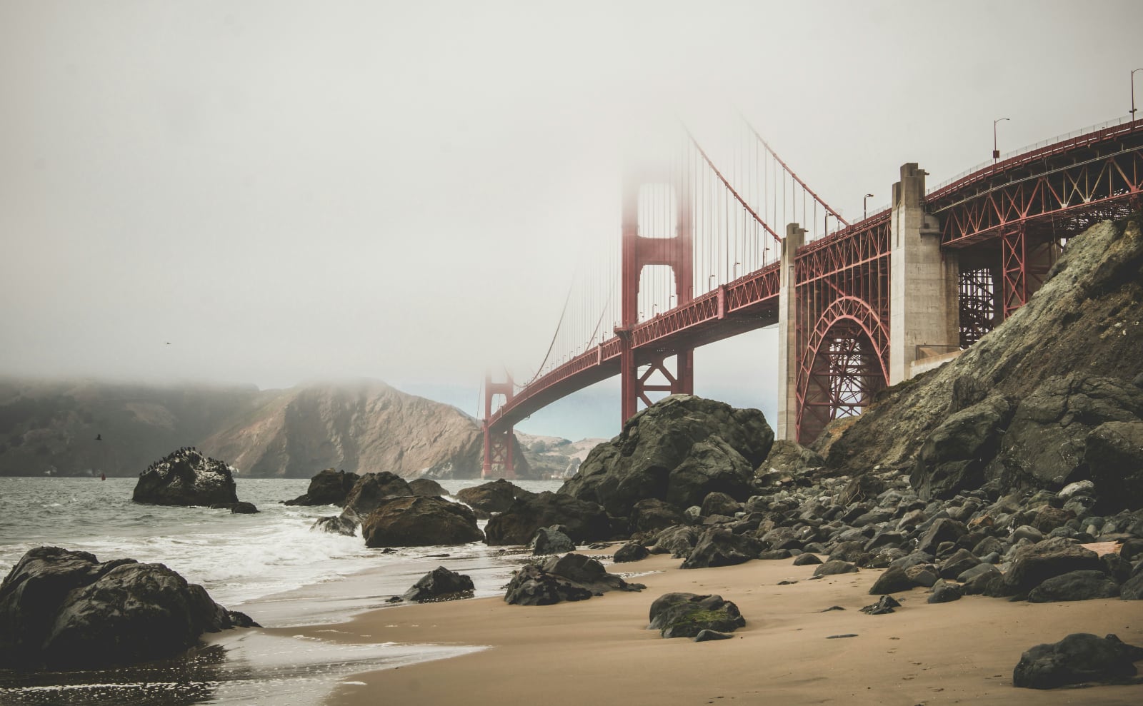 a view from under the golden gate bridge looking up at the arches from a sand beach