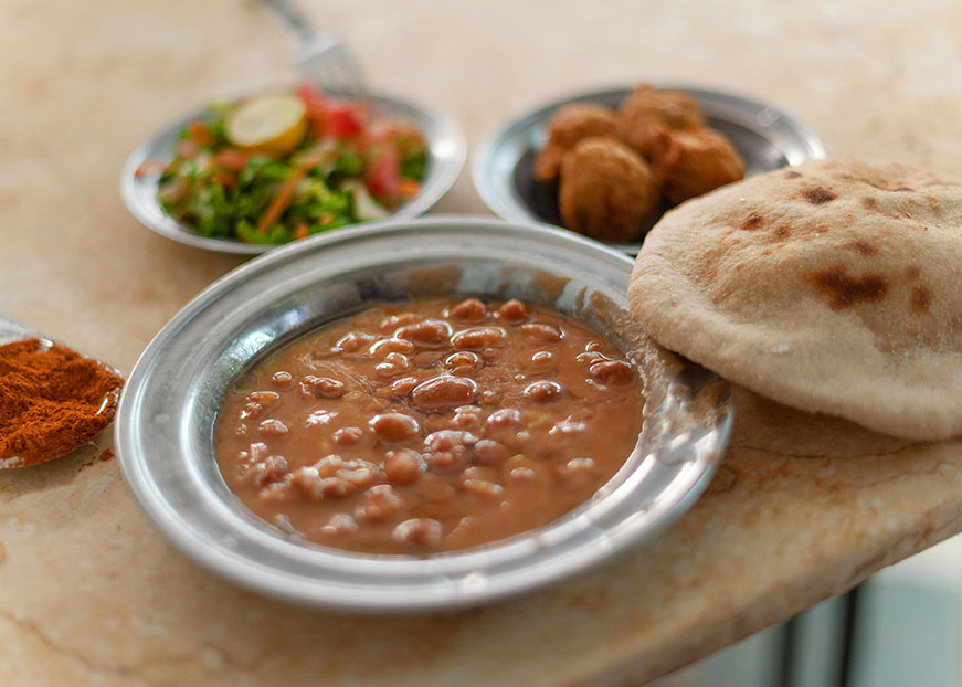a bowl of fava beans with pita bread on a table