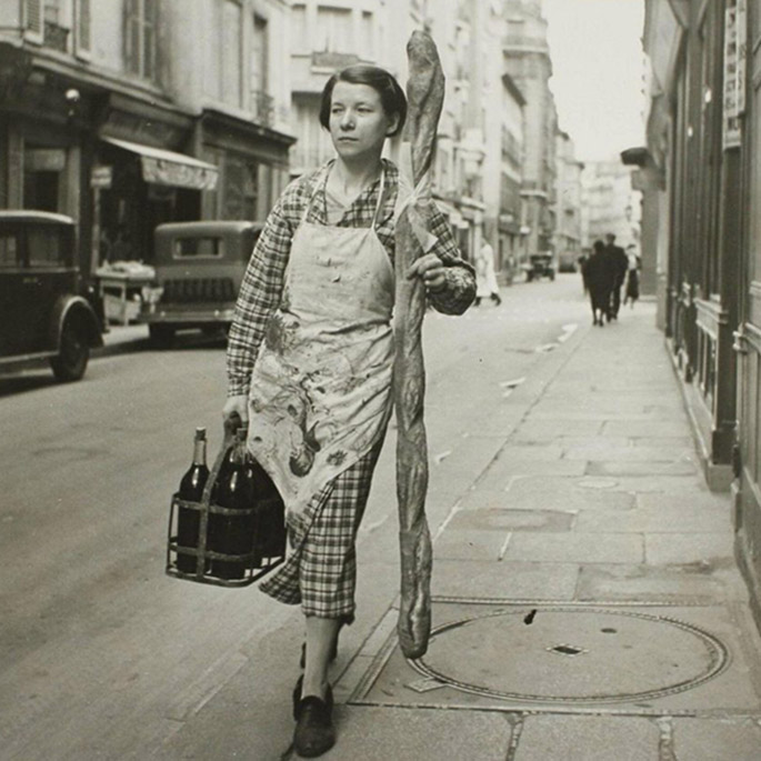black and white photo of a french woman carrying a 6-foot long baguette on a paris street