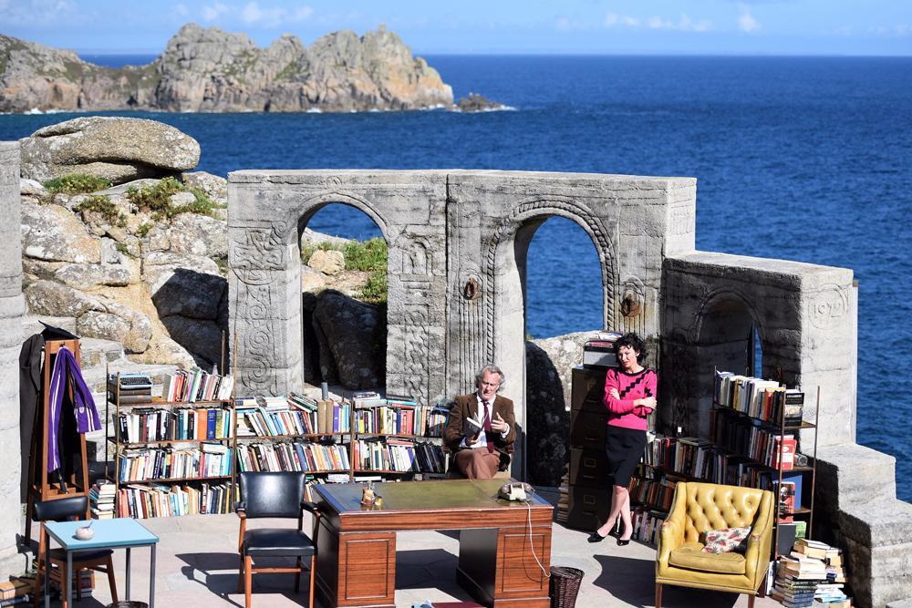  actors on a stage overlooking the ocean with bookshelves and easy chairs