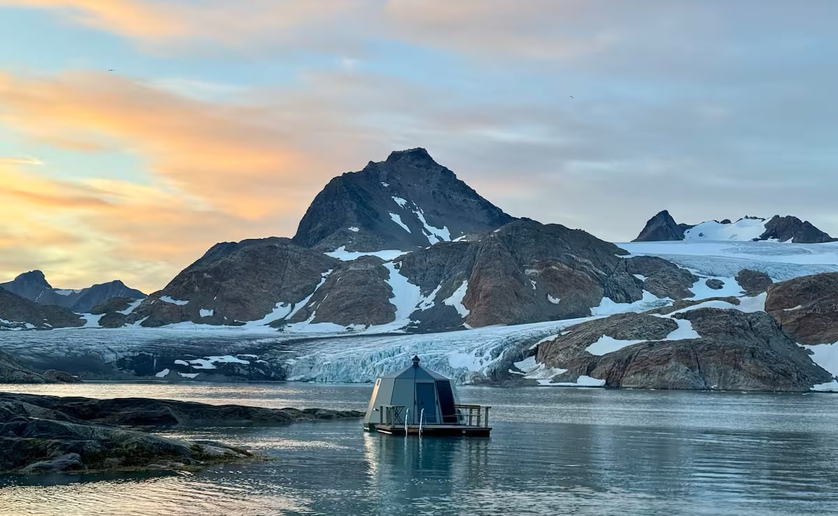 a hexagonal hut floating on the water with a mountain and colorful sky in the background