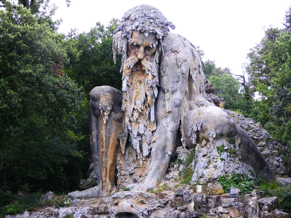 enormous stone sculpture of a man with a beard stepping out of a mountain in the forest