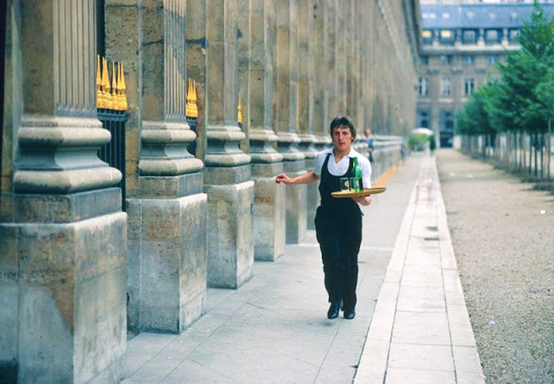 a waiter carries a serving tray down a street in paris