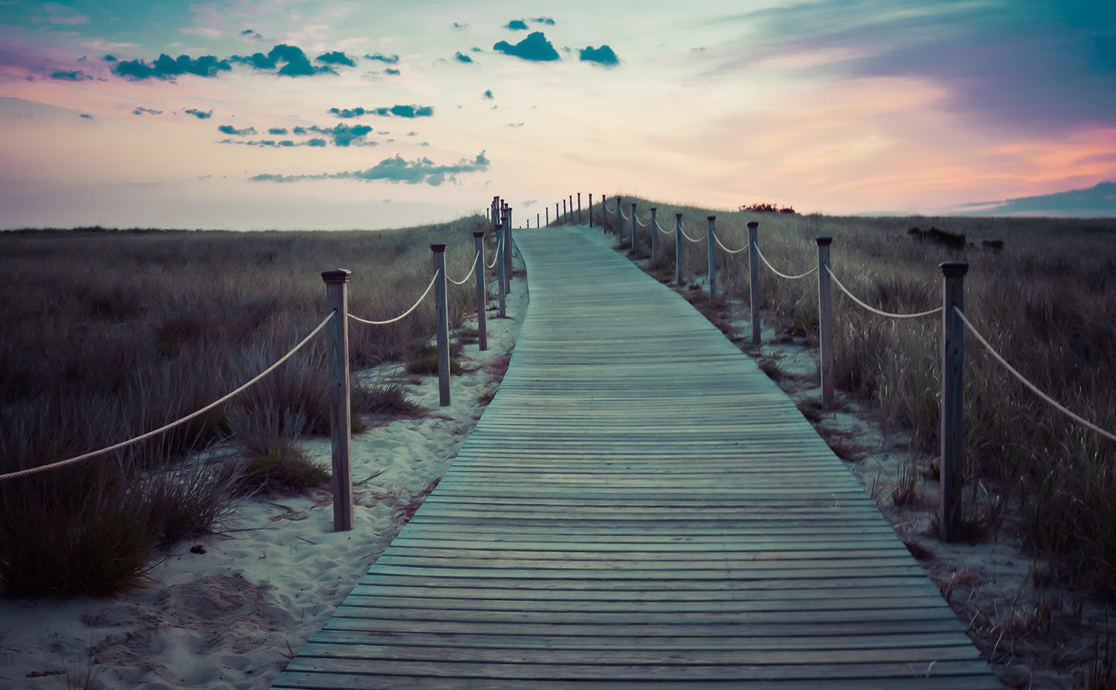 brown wooden boardwalk leading to the beach at sunset