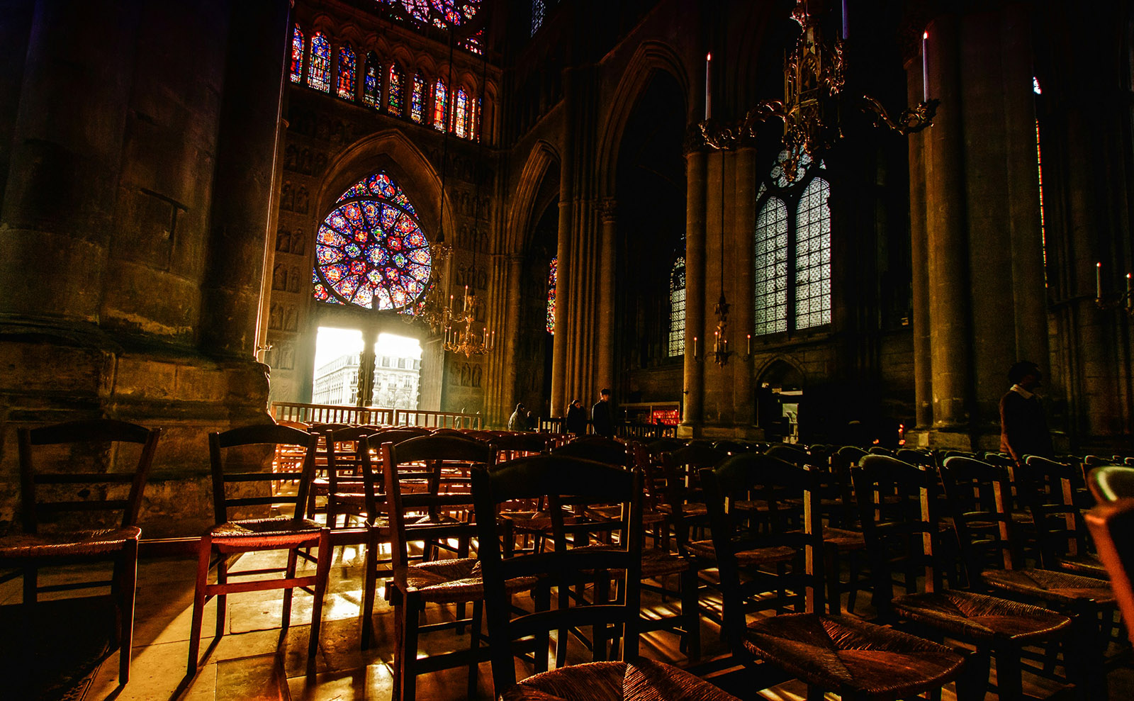 the inside of a dark church with brown wooden chairs and light shining through a round stained glass window