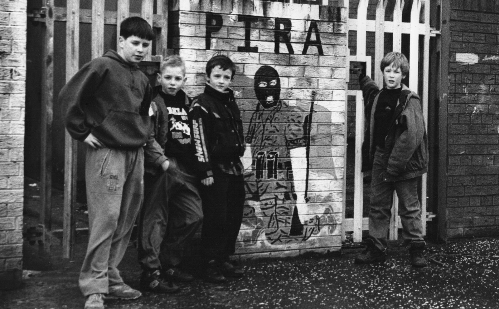 neighborhood kids posing with mural honoring members of provisional irish republican army in west belfast, northern ireland