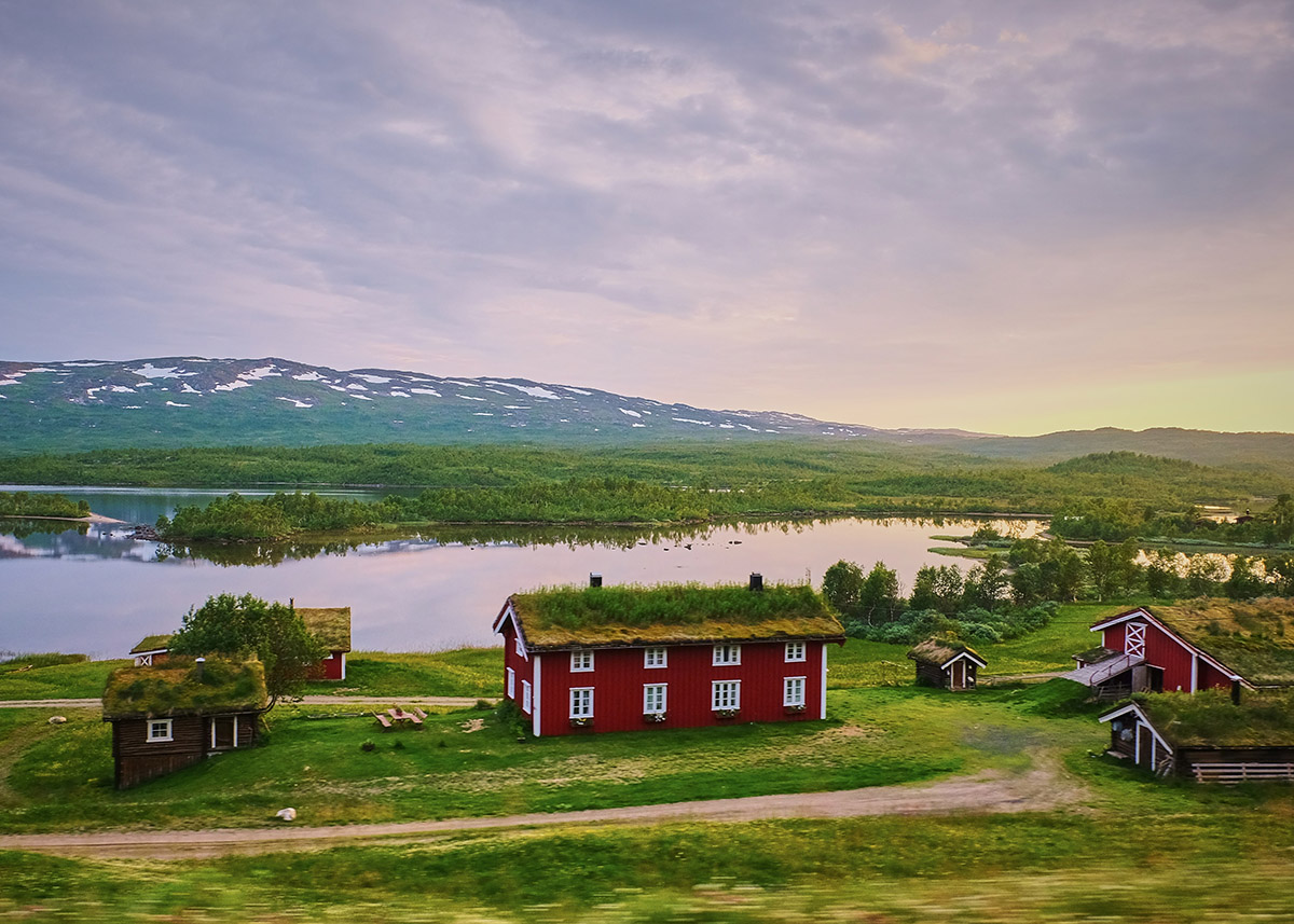 grassy fields with small red houses and hills in the background in sweden