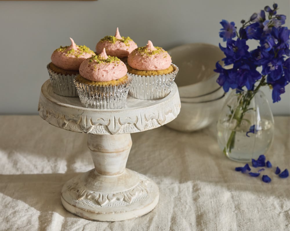 cupcakes with pink frosting on a tall white cake stand