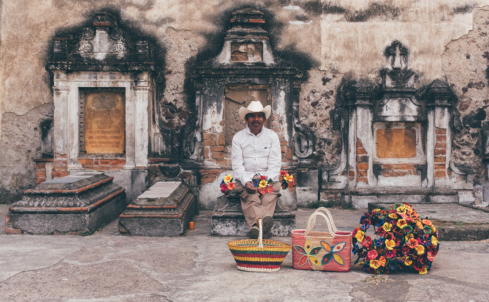 mexican man sitting with flowers in a cemetery
