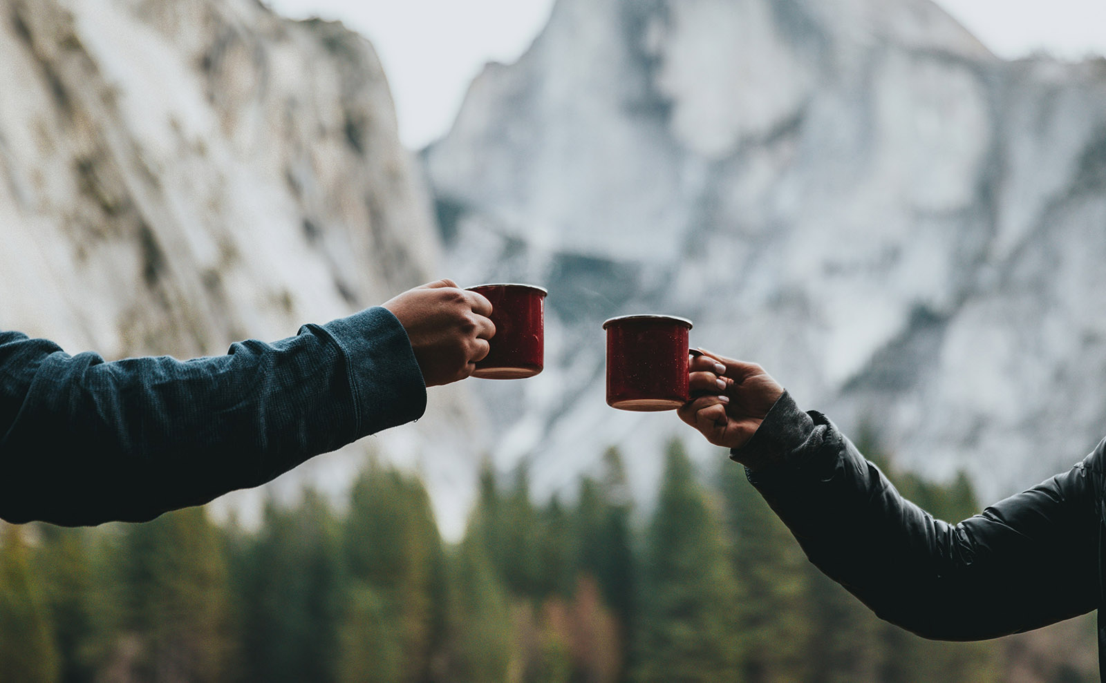 two people clinking red coffee cups together in front of a mountain
