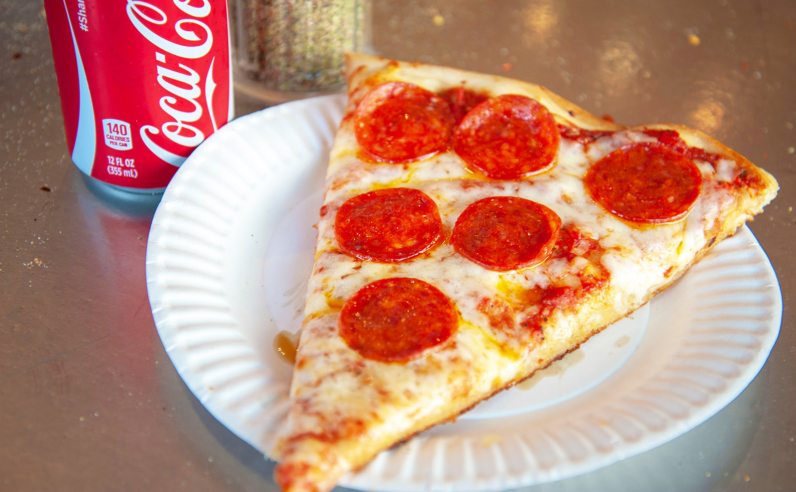 slice of pepperoni pizza on a paper plate with a can of coke